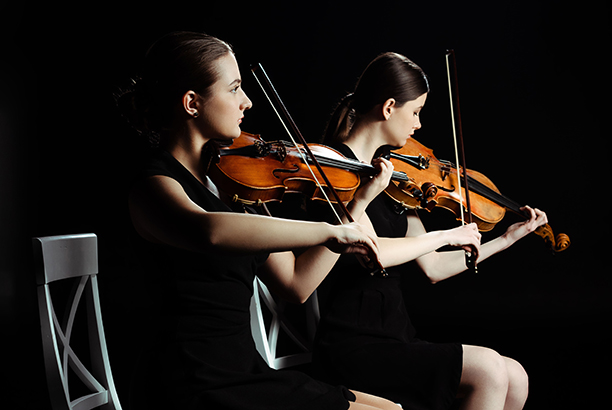 professional young musicians playing classical music on violins on dark stage